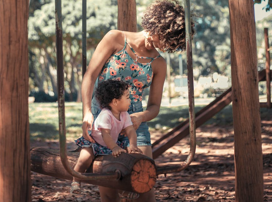 mother helping her baby girl ride a seesaw